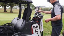 Man preparing golf clubs beside a golf cart on a golf course