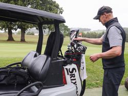 Man preparing golf clubs beside a golf cart on a golf course