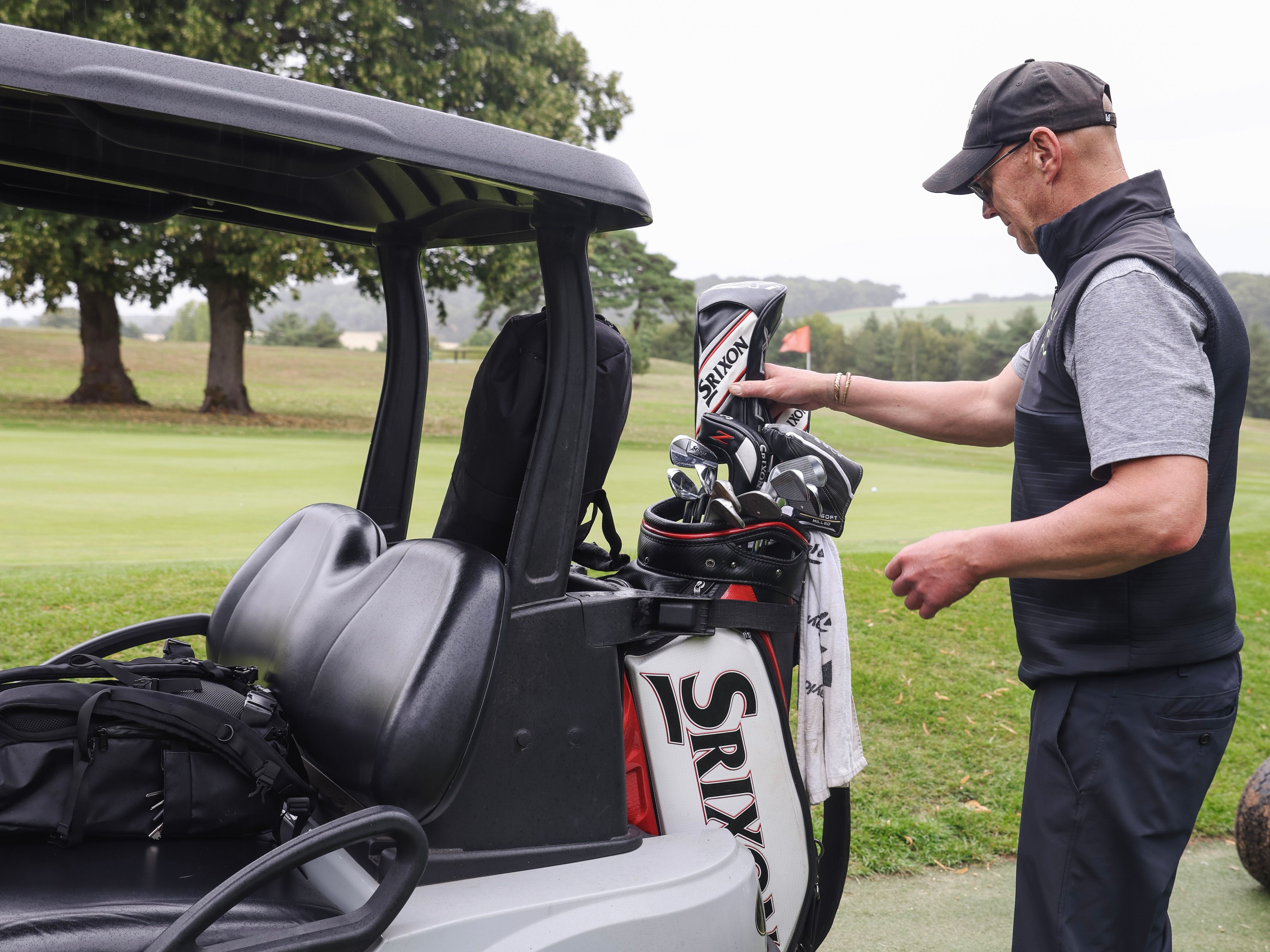 Man preparing golf clubs beside a golf cart on a golf course