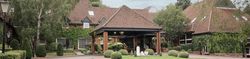 A large brick building with red tiled roof surrounded by lush greenery and manicured lawns.