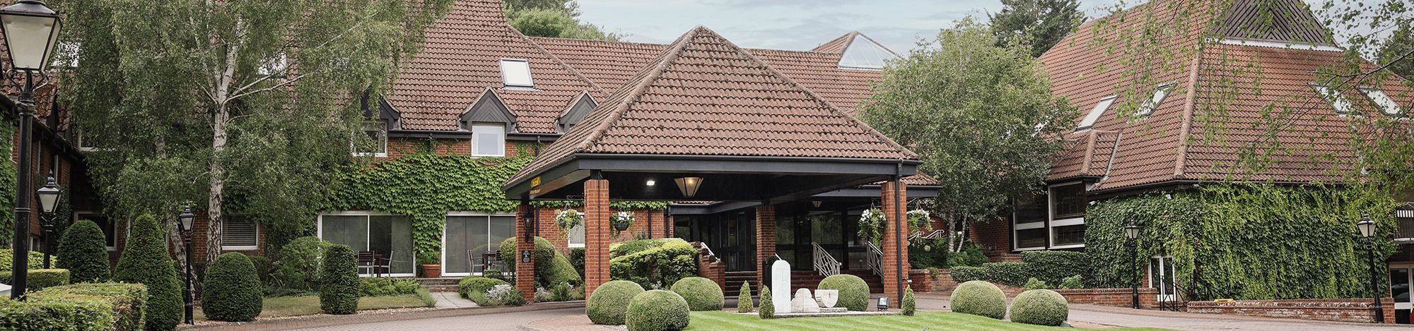 A large brick building with red tiled roof surrounded by lush greenery and manicured lawns.