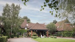 A large brick building with red tiled roof surrounded by lush greenery and manicured lawns.