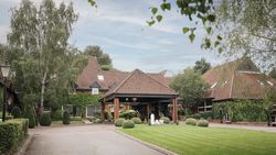 A large brick building with red tiled roof surrounded by lush greenery and manicured lawns.