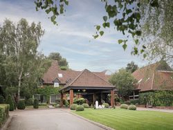 A large brick building with red tiled roof surrounded by lush greenery and manicured lawns.