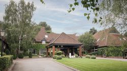 A large brick building with red tiled roof surrounded by lush greenery and manicured lawns.