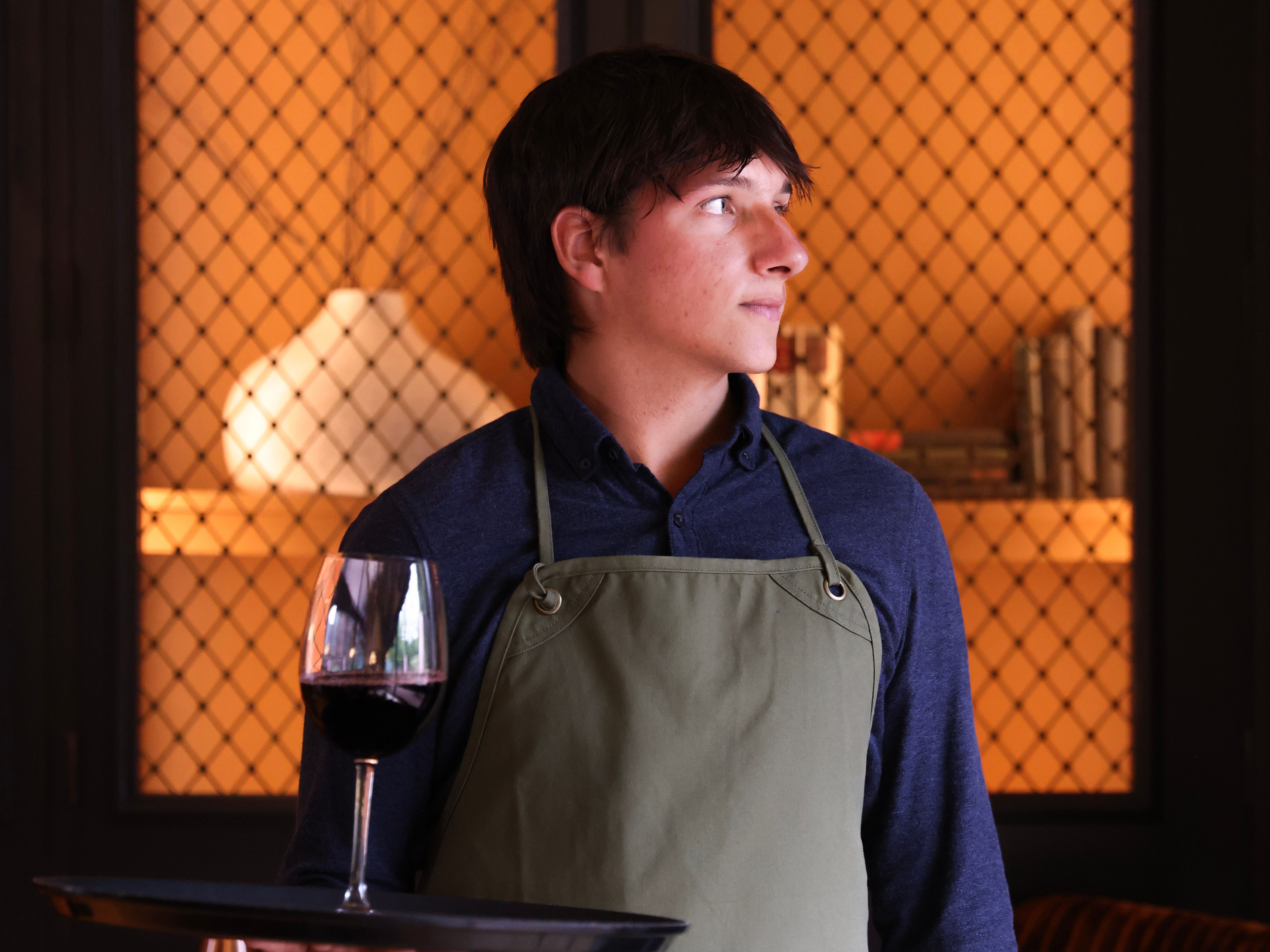 Waiter holding a tray with a glass of red wine in a cozy, warmly lit room