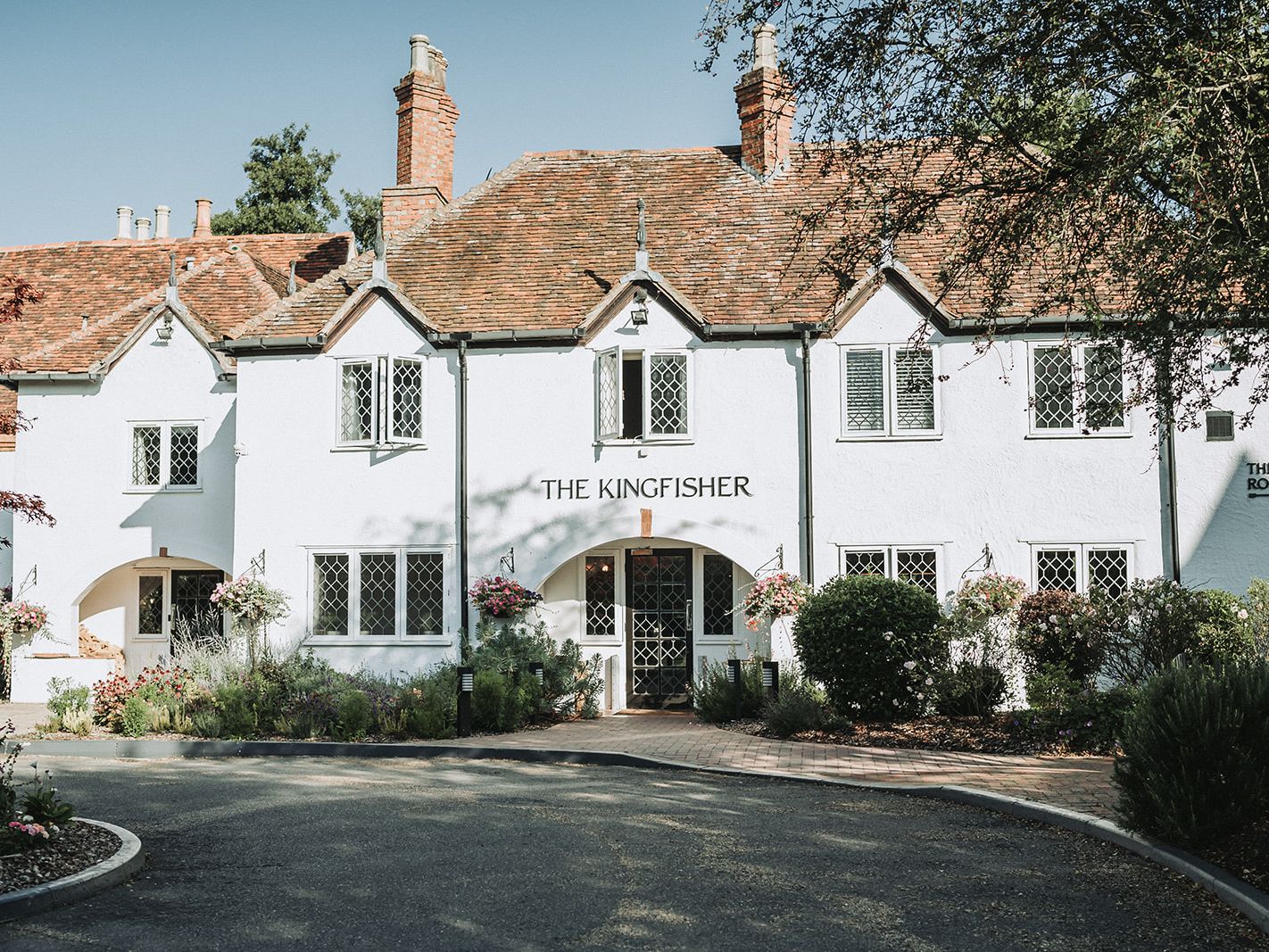The front exterior of The Kingfisher, a charming white inn with a red tiled roof and greenery.