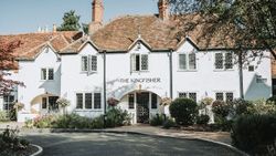 The front exterior of The Kingfisher, a charming white inn with a red tiled roof and greenery.
