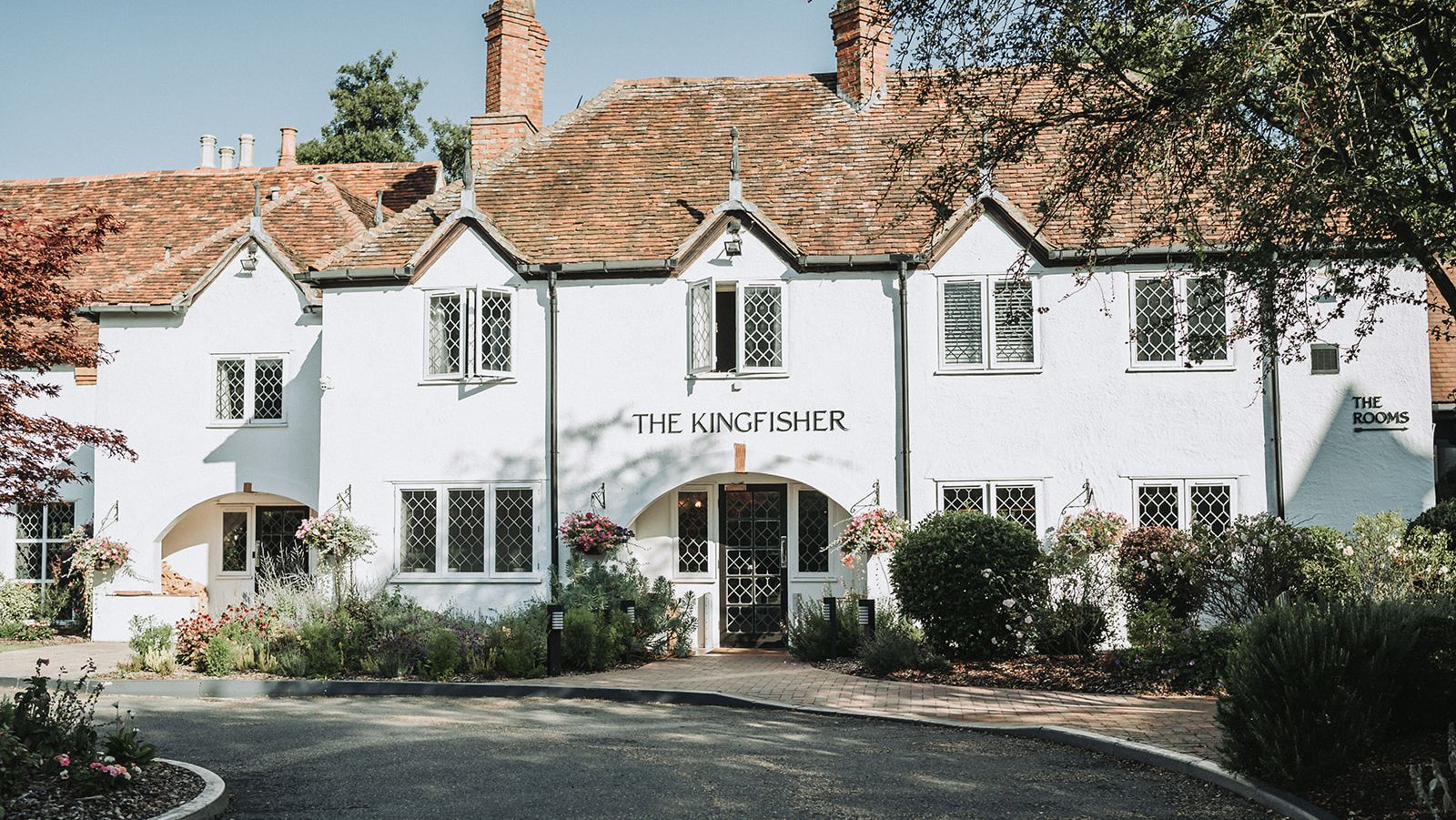 The front exterior of The Kingfisher, a charming white inn with a red tiled roof and greenery.