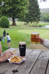 Drinks and potato chips on a wooden table with a golfing green in the background