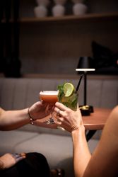 Two people clinking cocktails in a dimly lit lounge setting