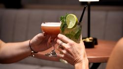 Two people clinking cocktails in a dimly lit lounge setting