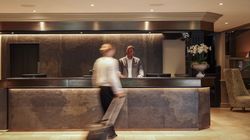 Hotel lobby reception desk with a receptionist standing behind the counter and a guest walking by with luggage.