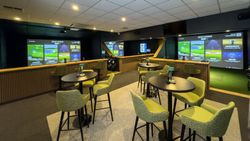 Modern indoor golf simulator lounge with large screens and green chairs