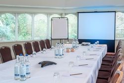 Conference room setup with a U-shaped table, chairs, water bottles, notepads, projector screen, and flip chart.