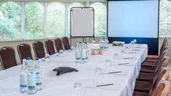Conference room setup with a U-shaped table, chairs, water bottles, notepads, projector screen, and flip chart.