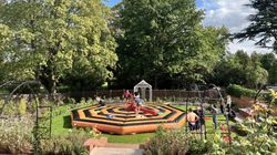 People playing on an inflatable game in a garden with large trees and a gazebo in the background.