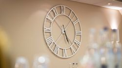Large wall clock with Roman numerals, bottles blurred in foreground