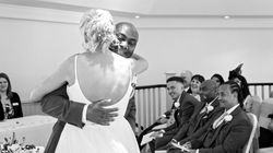 Bride and groom embrace during a wedding ceremony, with smiling guests seated and watching.