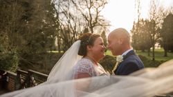 Bride and groom smiling at each other outdoors with veil blowing in the wind