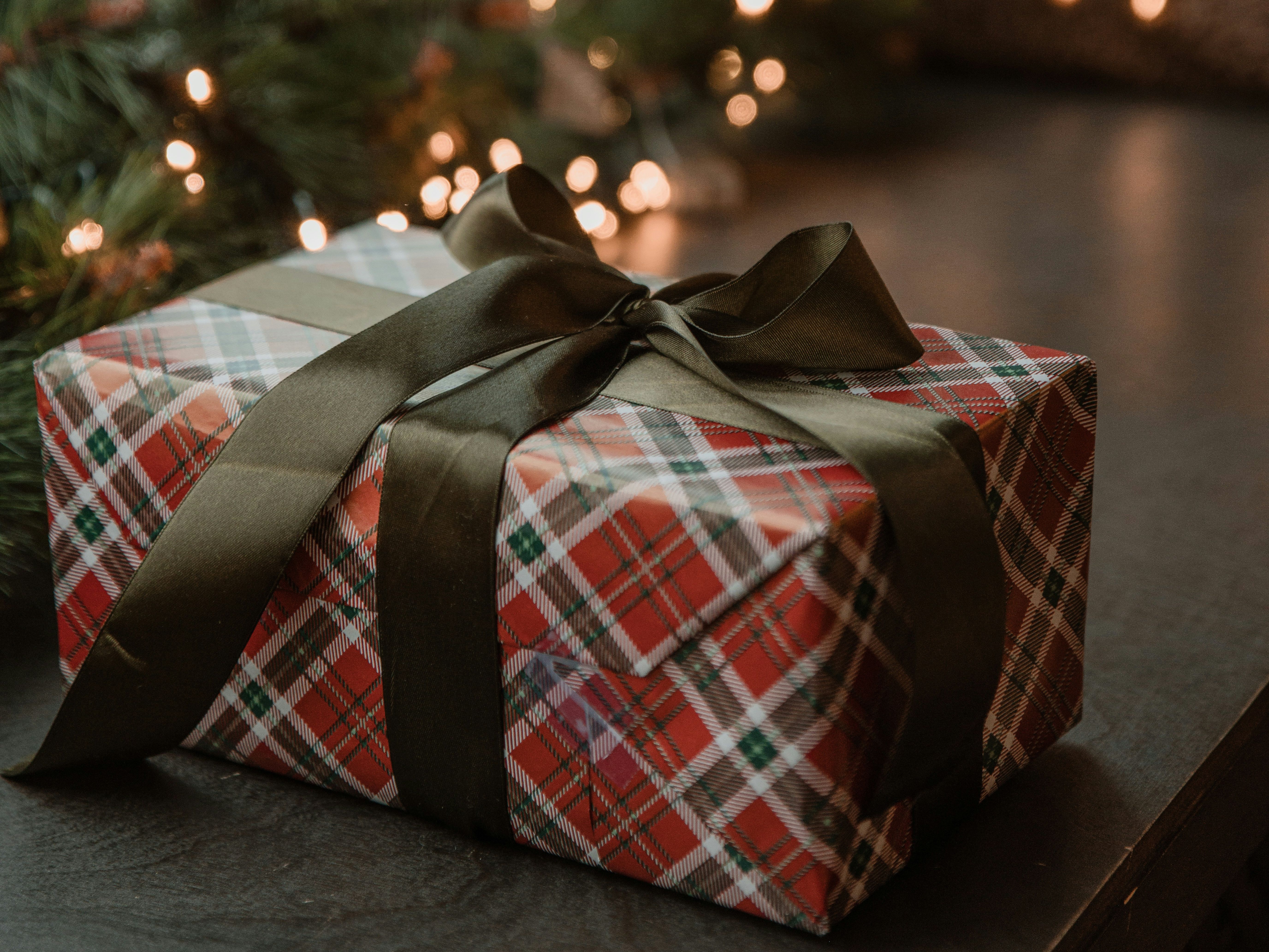 Plaid-wrapped gift box with dark ribbon on a table near holiday lights