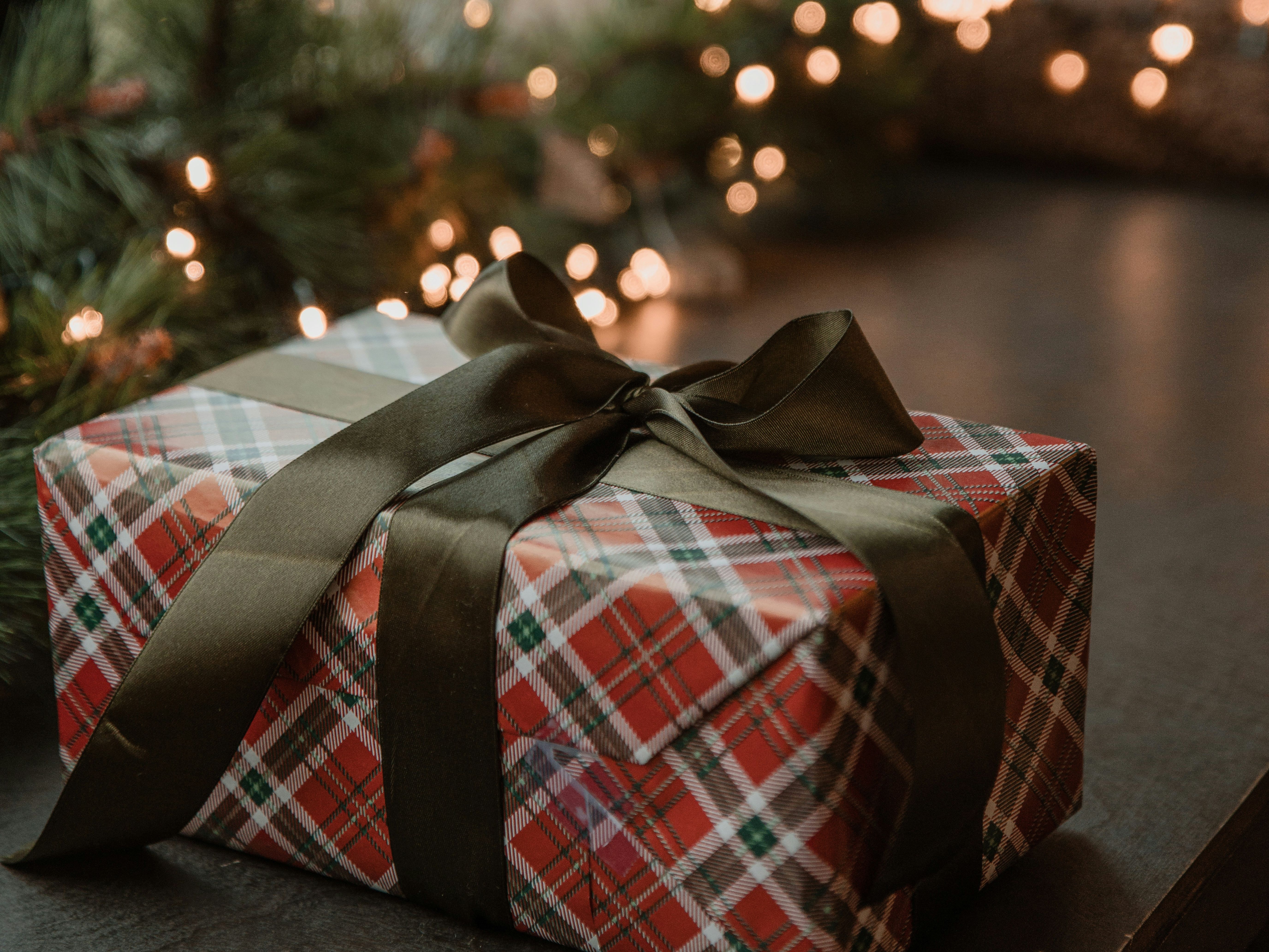 Plaid-wrapped gift box with dark ribbon on a table near holiday lights