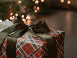 Plaid-wrapped gift box with dark ribbon on a table near holiday lights