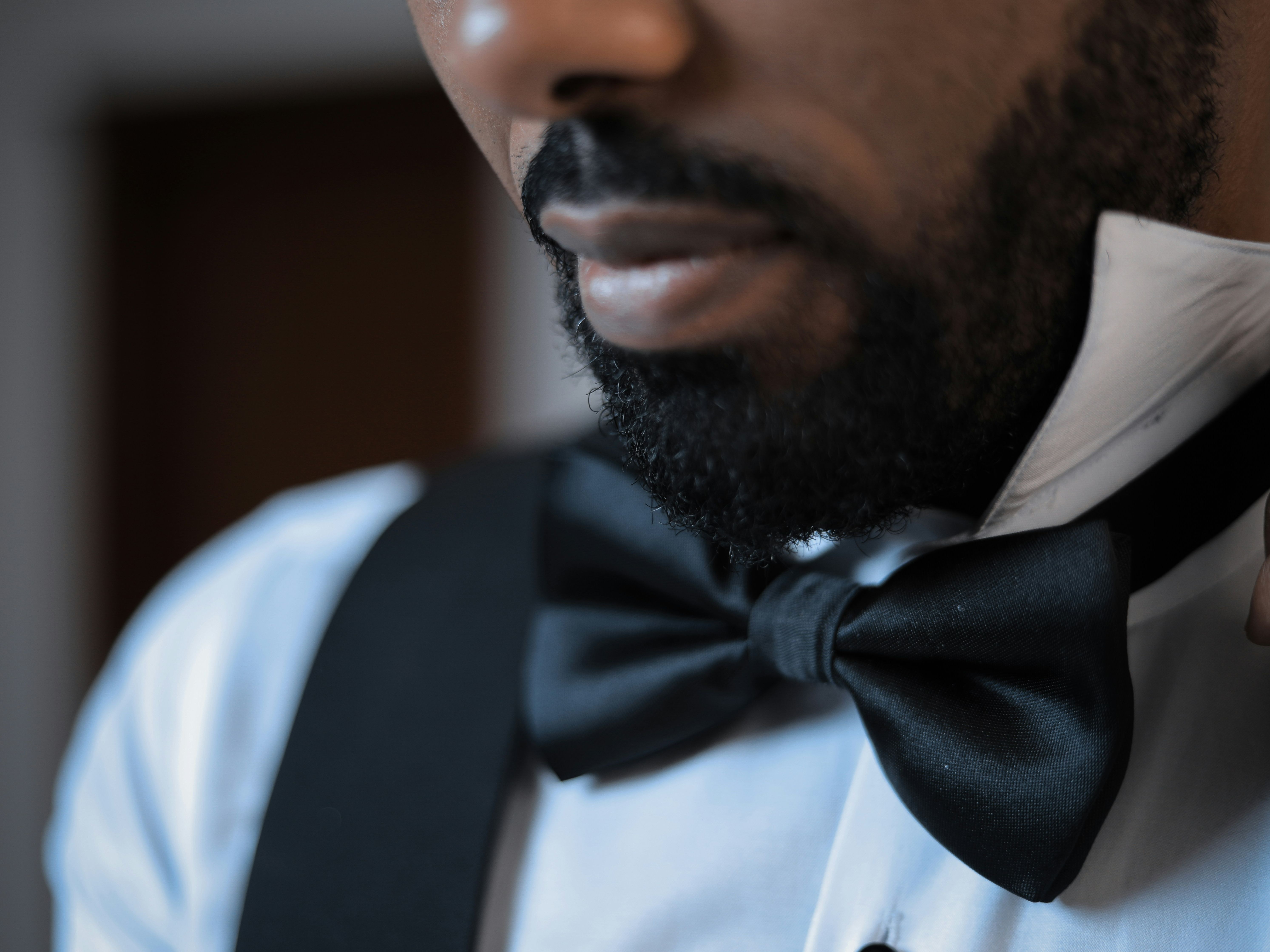 Close-up of a man with a beard adjusting his black bow tie and white dress shirt.