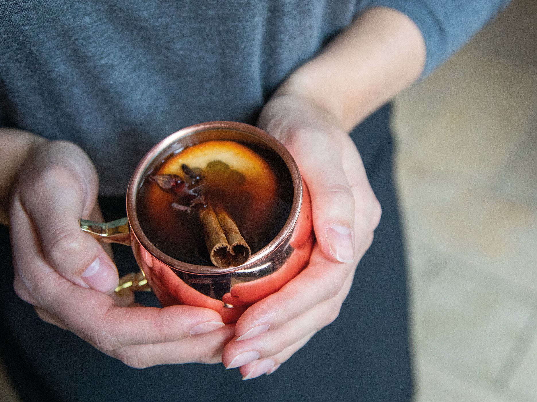 Person holding a copper mug with mulled wine garnished with orange slice and cinnamon stick