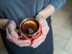 Person holding a copper mug with mulled wine garnished with orange slice and cinnamon stick