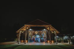 Wooden barn-style building illuminated at night with people visible inside through large glass doors.