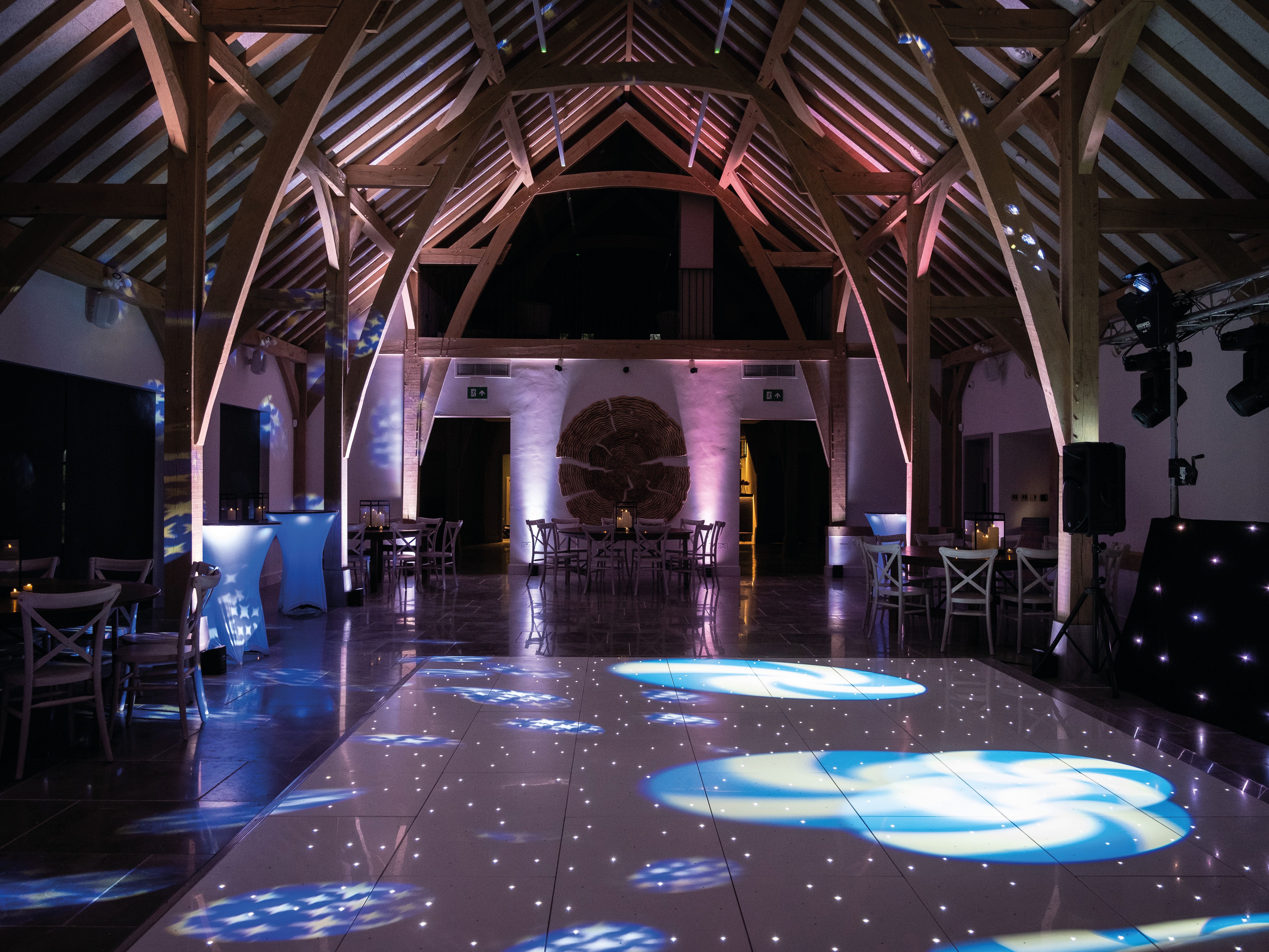 Empty event venue with wooden beams and colorful lights projected onto the dance floor.