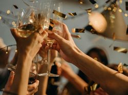 People cheering with wine glasses at a festive celebration with golden confetti.