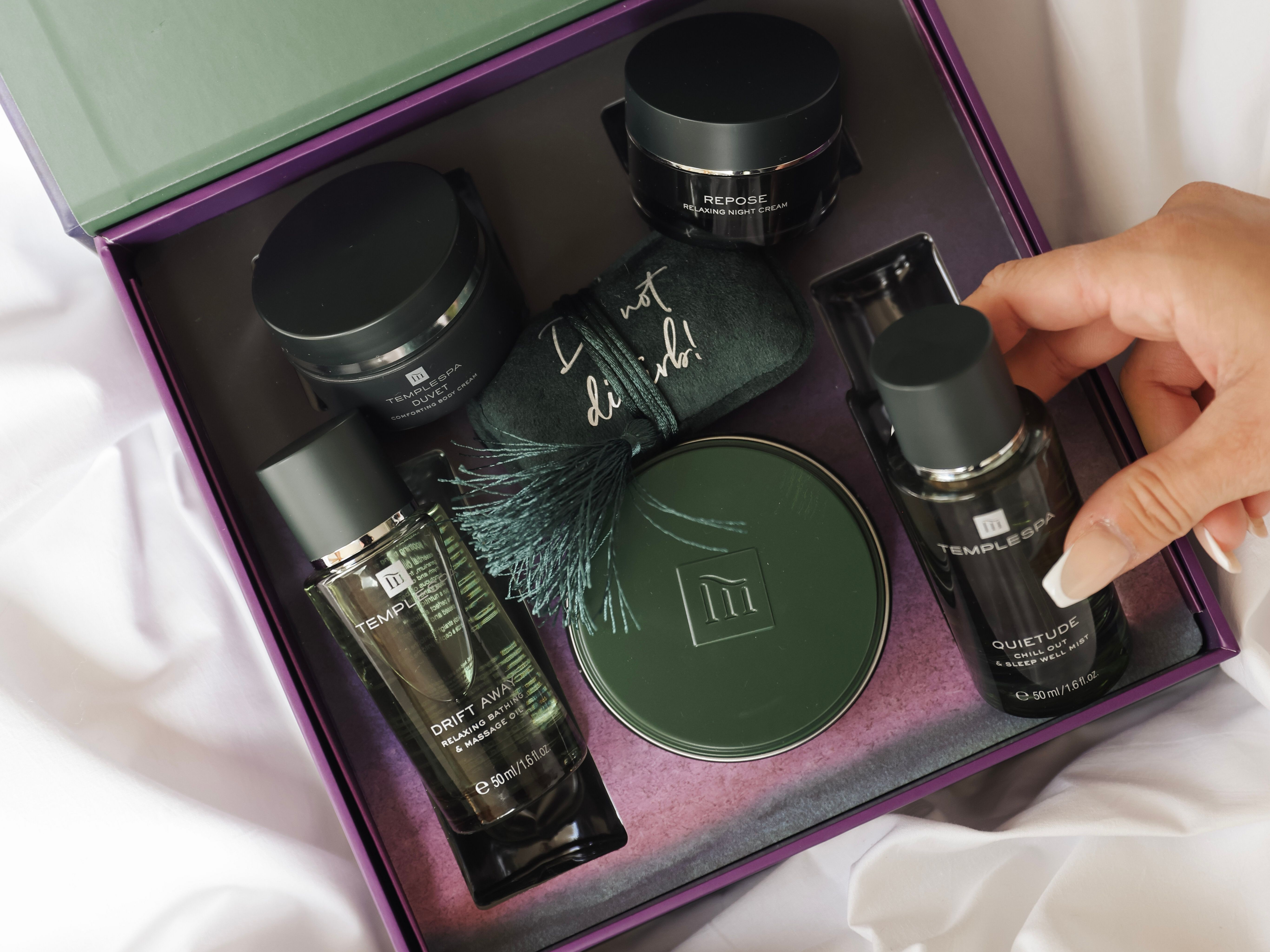 Luxury self-care gift set with various skincare products and a hand reaching for a bottle