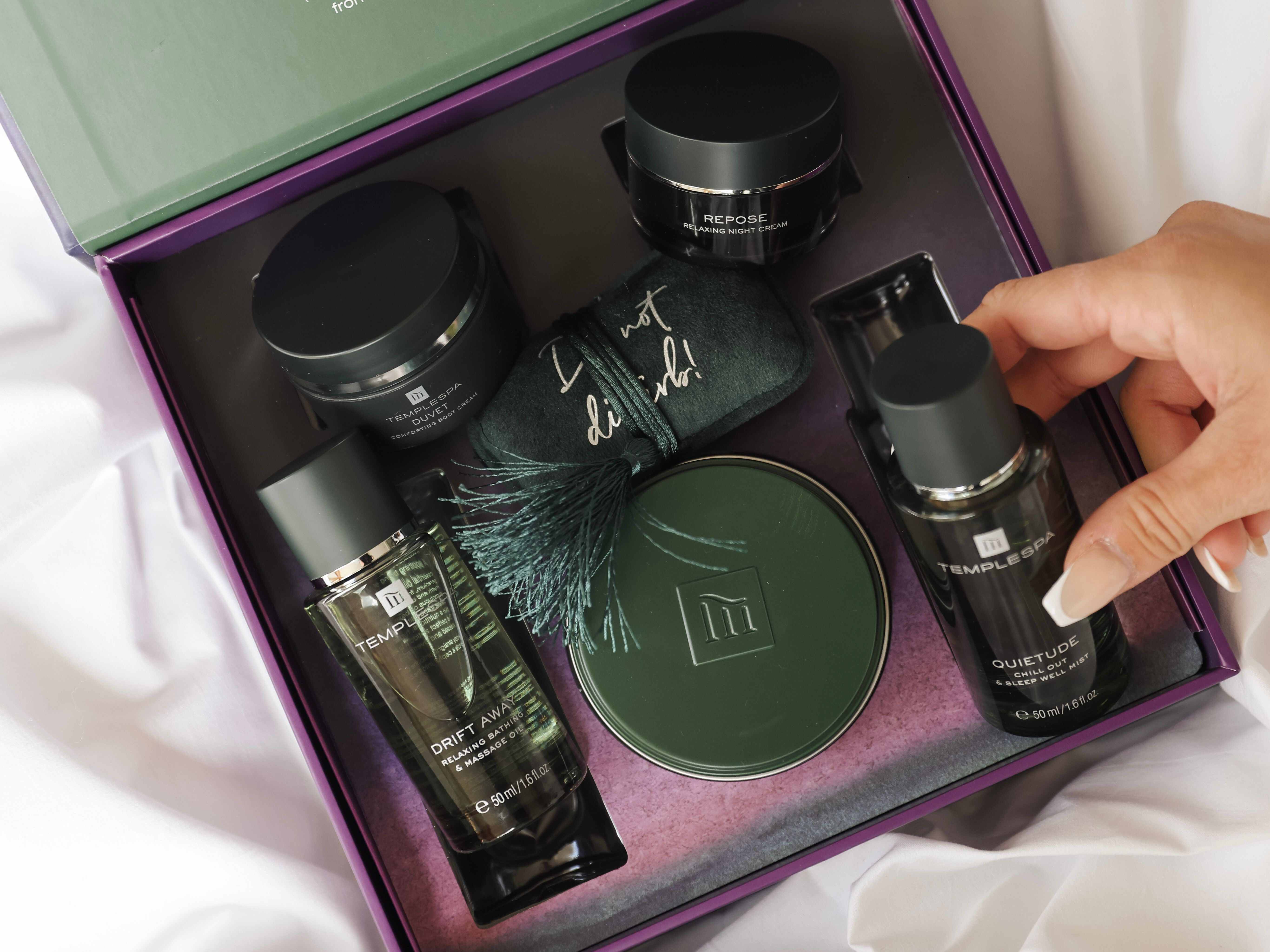Luxury self-care gift set with various skincare products and a hand reaching for a bottle