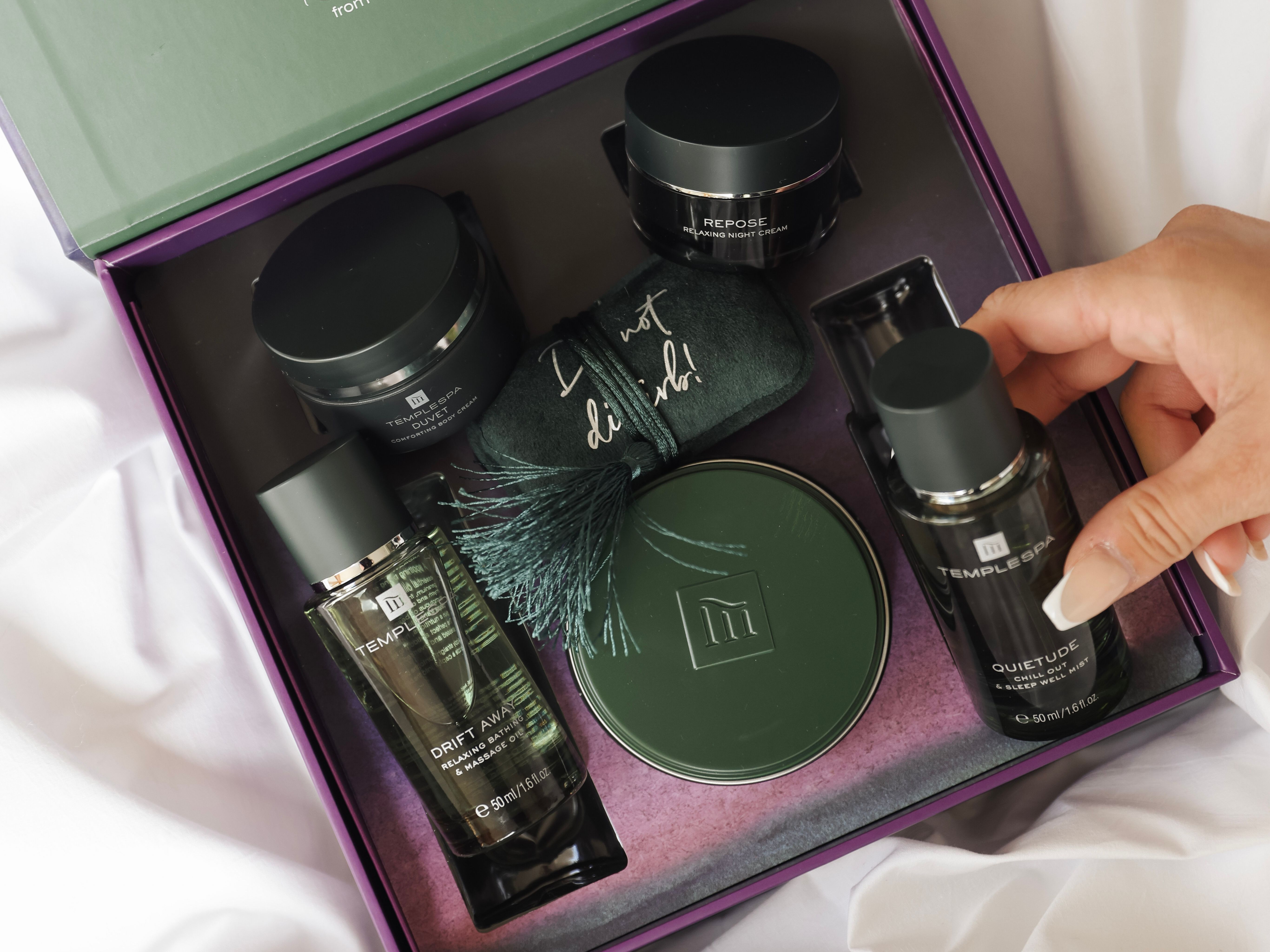 Luxury self-care gift set with various skincare products and a hand reaching for a bottle