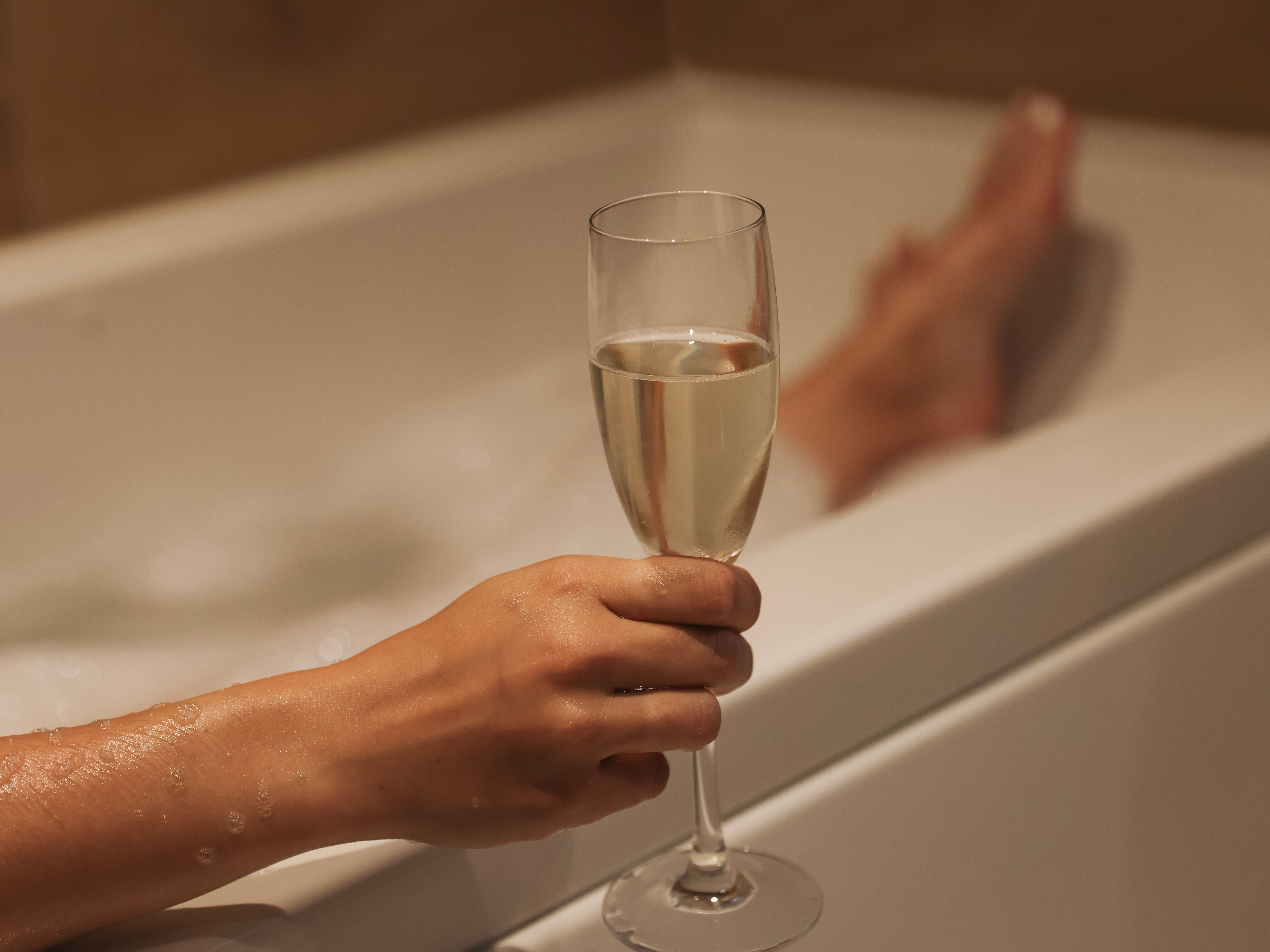 Person holding a glass of champagne while relaxing in a bathtub
