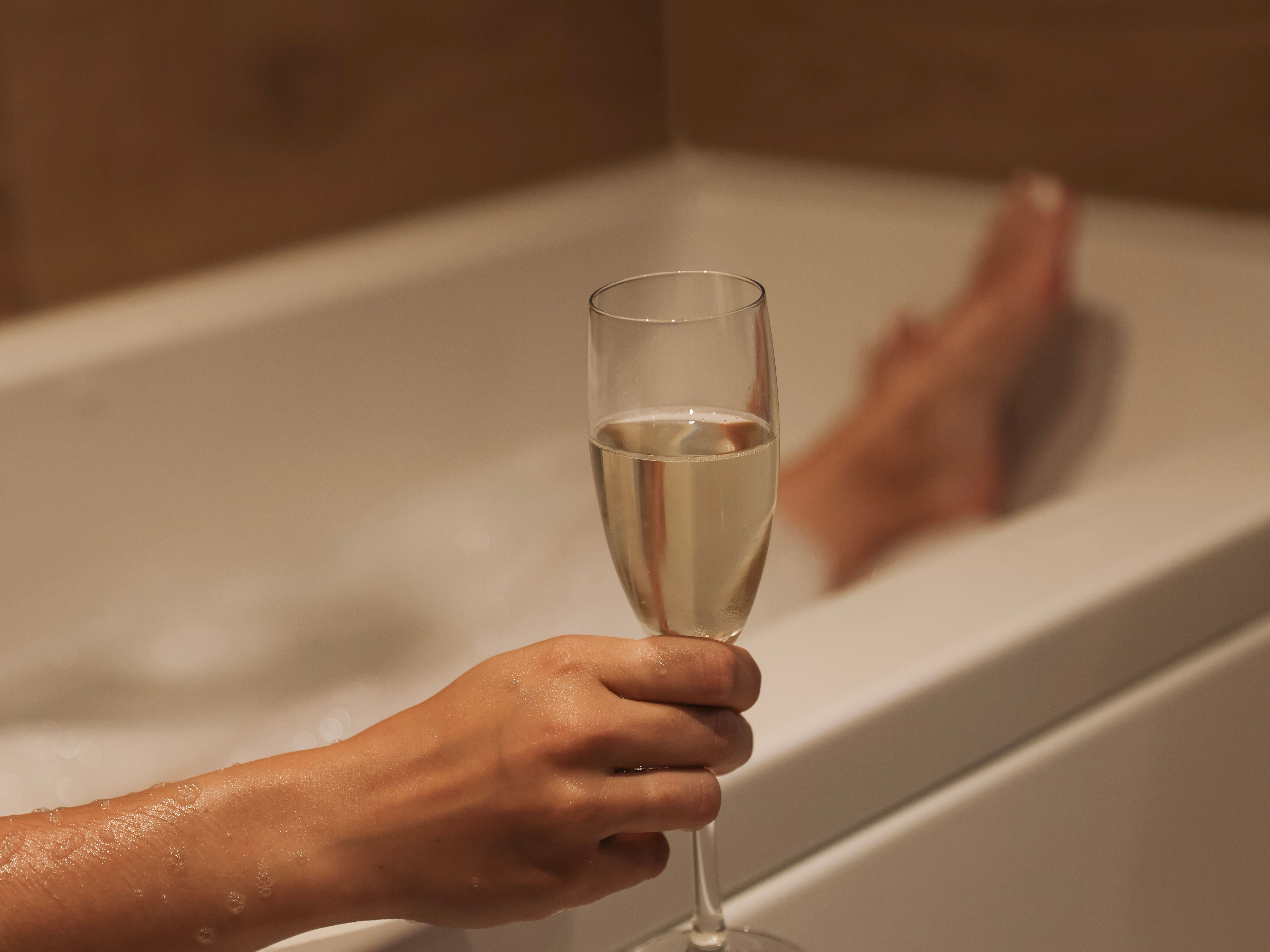 Person holding a glass of champagne while relaxing in a bathtub
