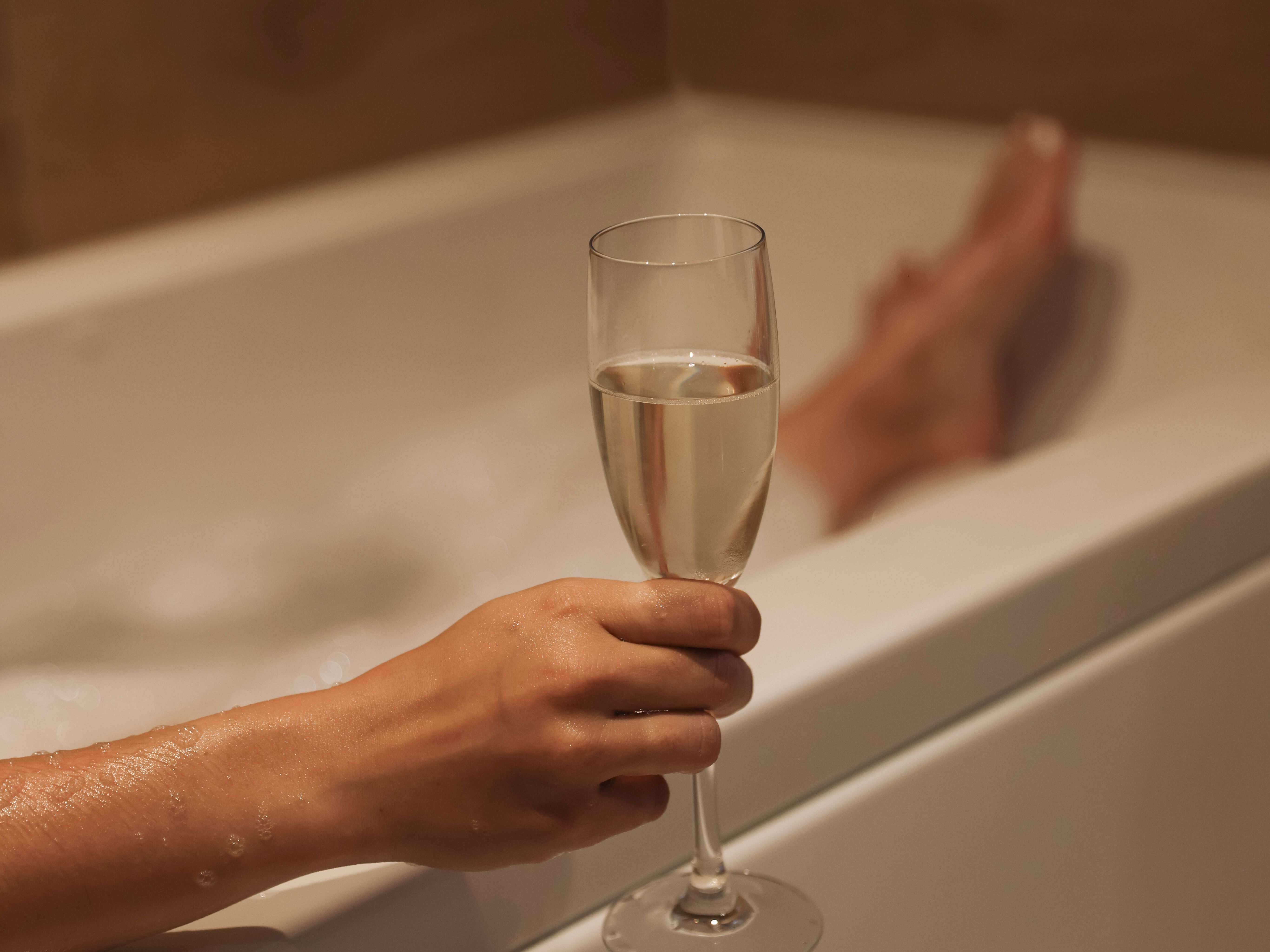 Person holding a glass of champagne while relaxing in a bathtub