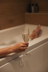 Person holding a glass of champagne while relaxing in a bathtub