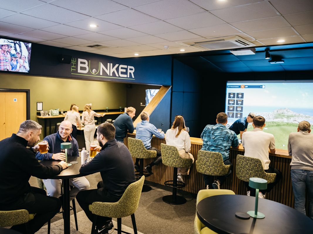 People socializing and playing golf simulator at The Bunker indoor venue.