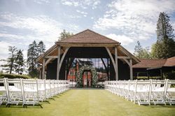 Outdoor wedding ceremony setup with white chairs and a floral arch under a wooden pavilion