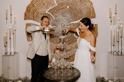 Bride and groom pouring champagne into a tower of glasses at their wedding reception.