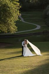 Bride and groom kissing outdoors with bride's veil flowing in the sunlight