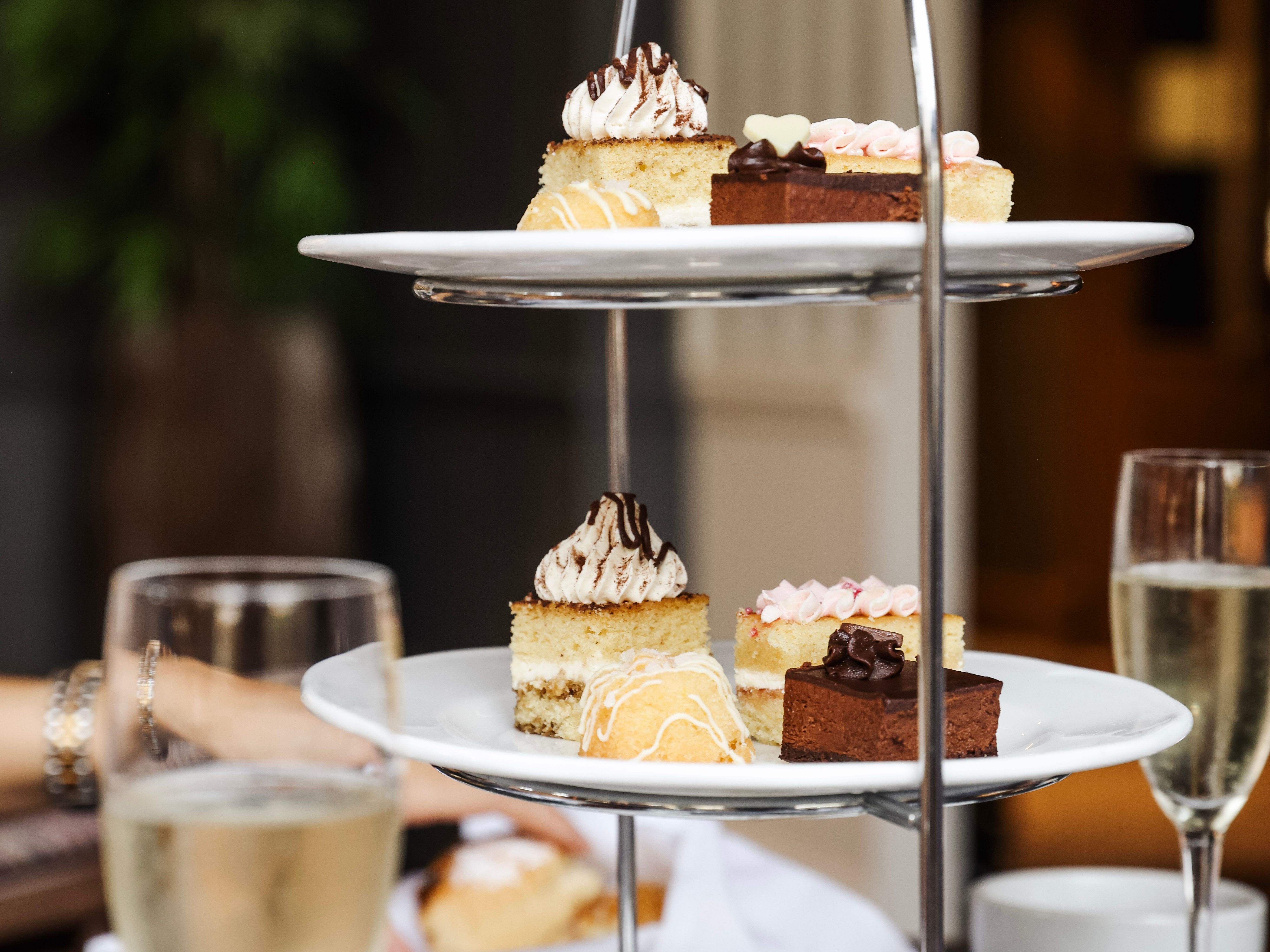 Three-tiered stand with assorted pastries and sandwiches, surrounded by cups and glasses of sparkling wine.