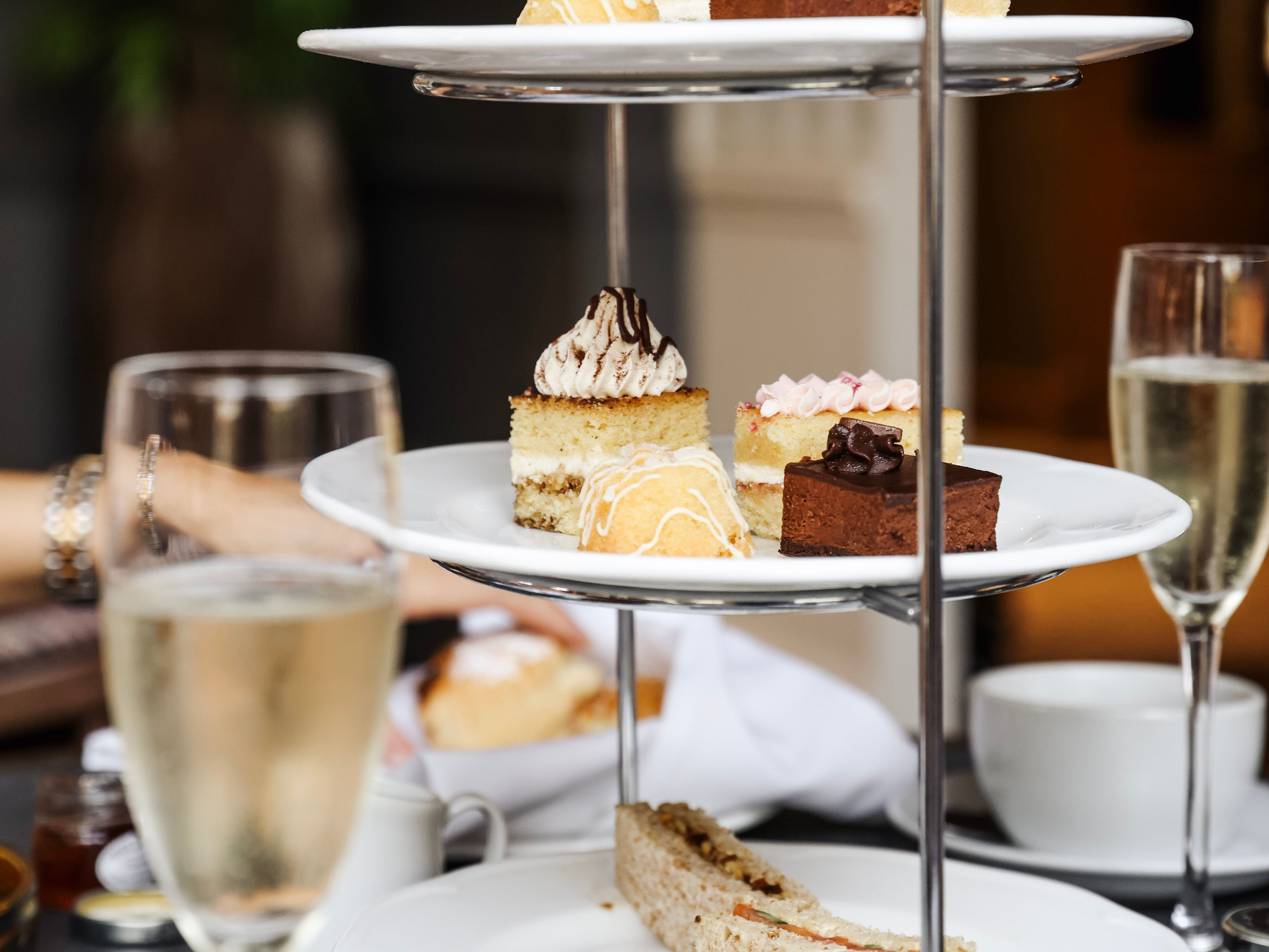 Three-tiered stand with assorted pastries and sandwiches, surrounded by cups and glasses of sparkling wine.