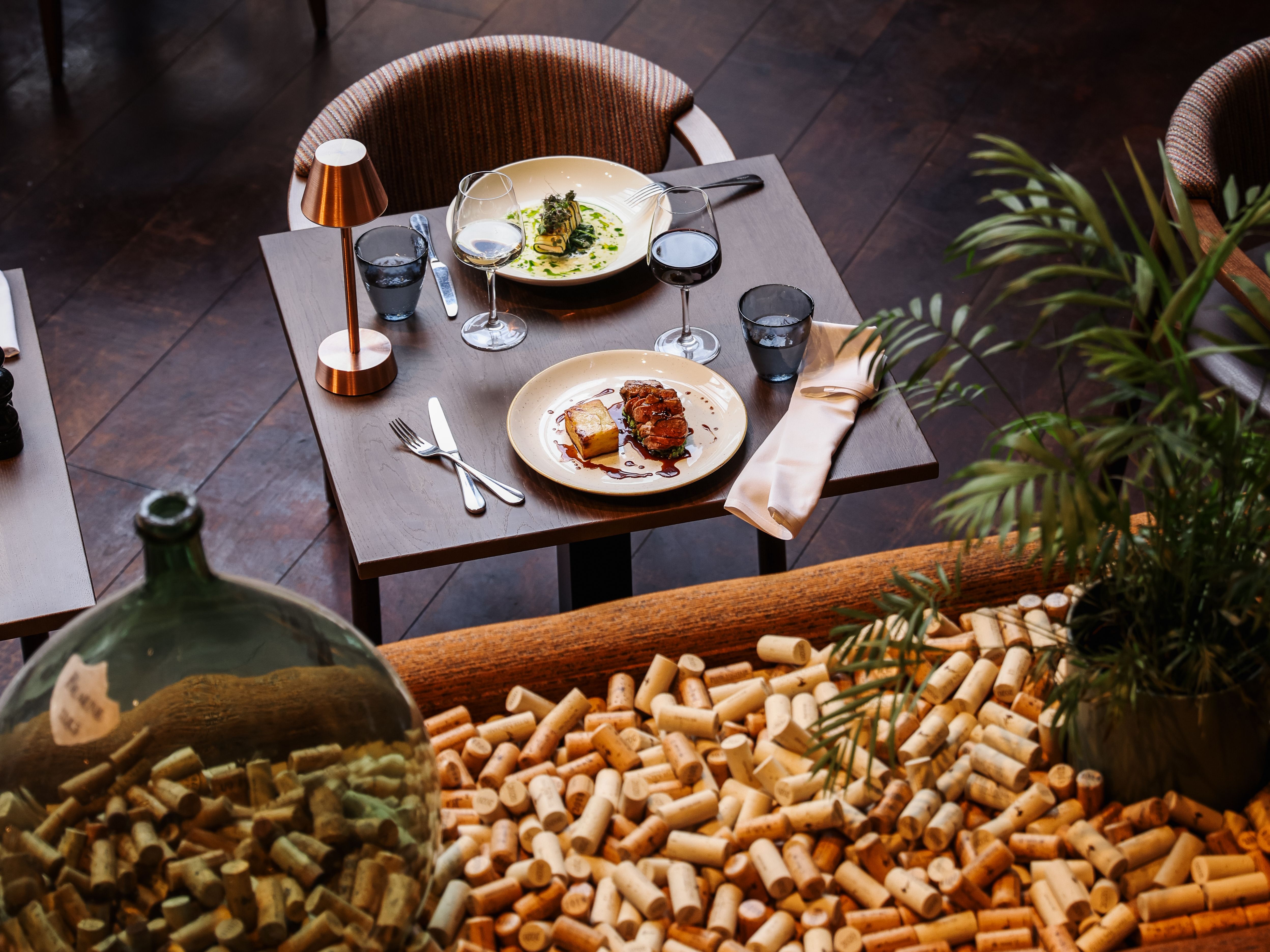 Elegant restaurant table set for two with gourmet dishes, wine glasses, and a background of wine corks.