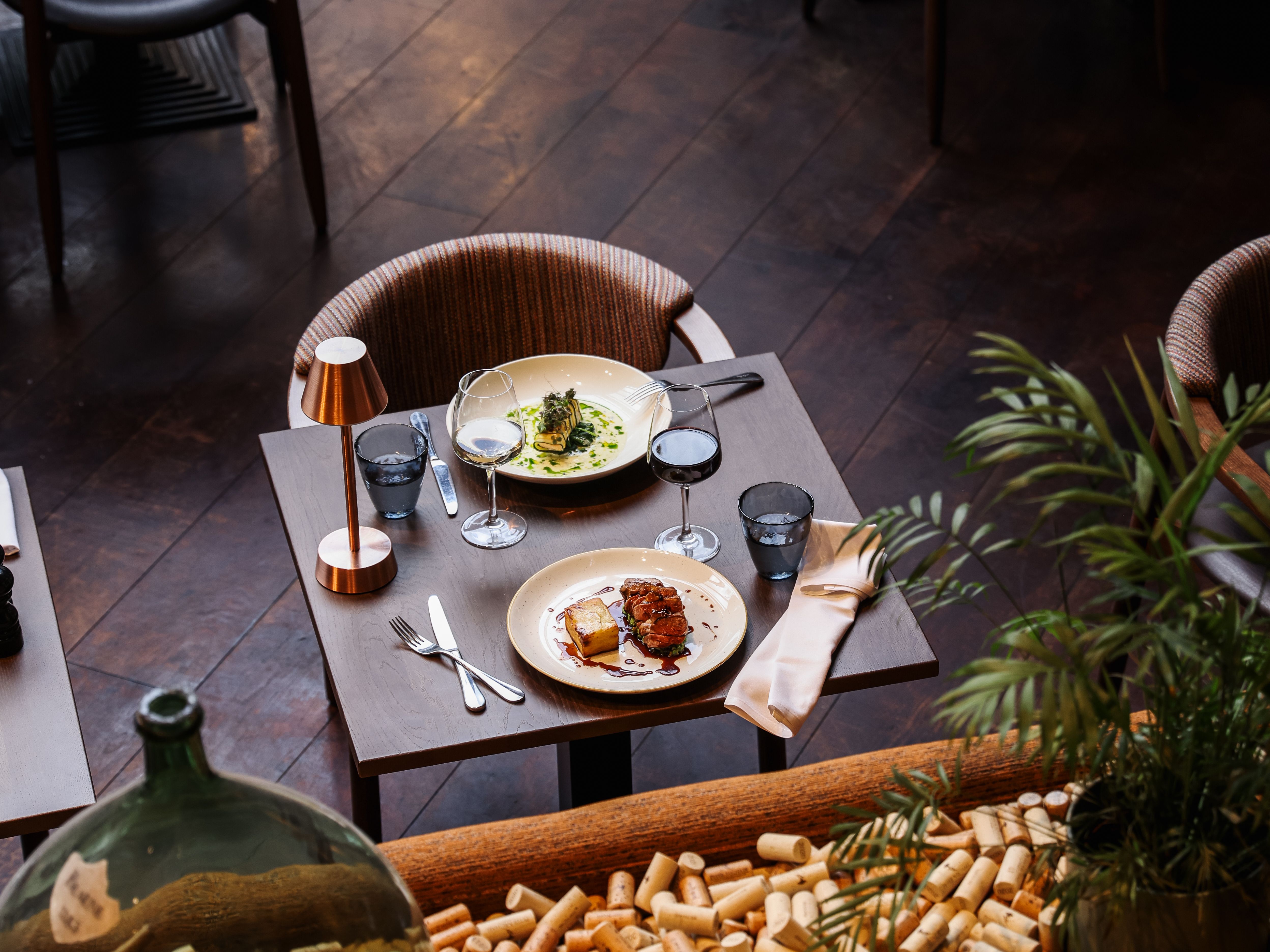 Elegant restaurant table set for two with gourmet dishes, wine glasses, and a background of wine corks.