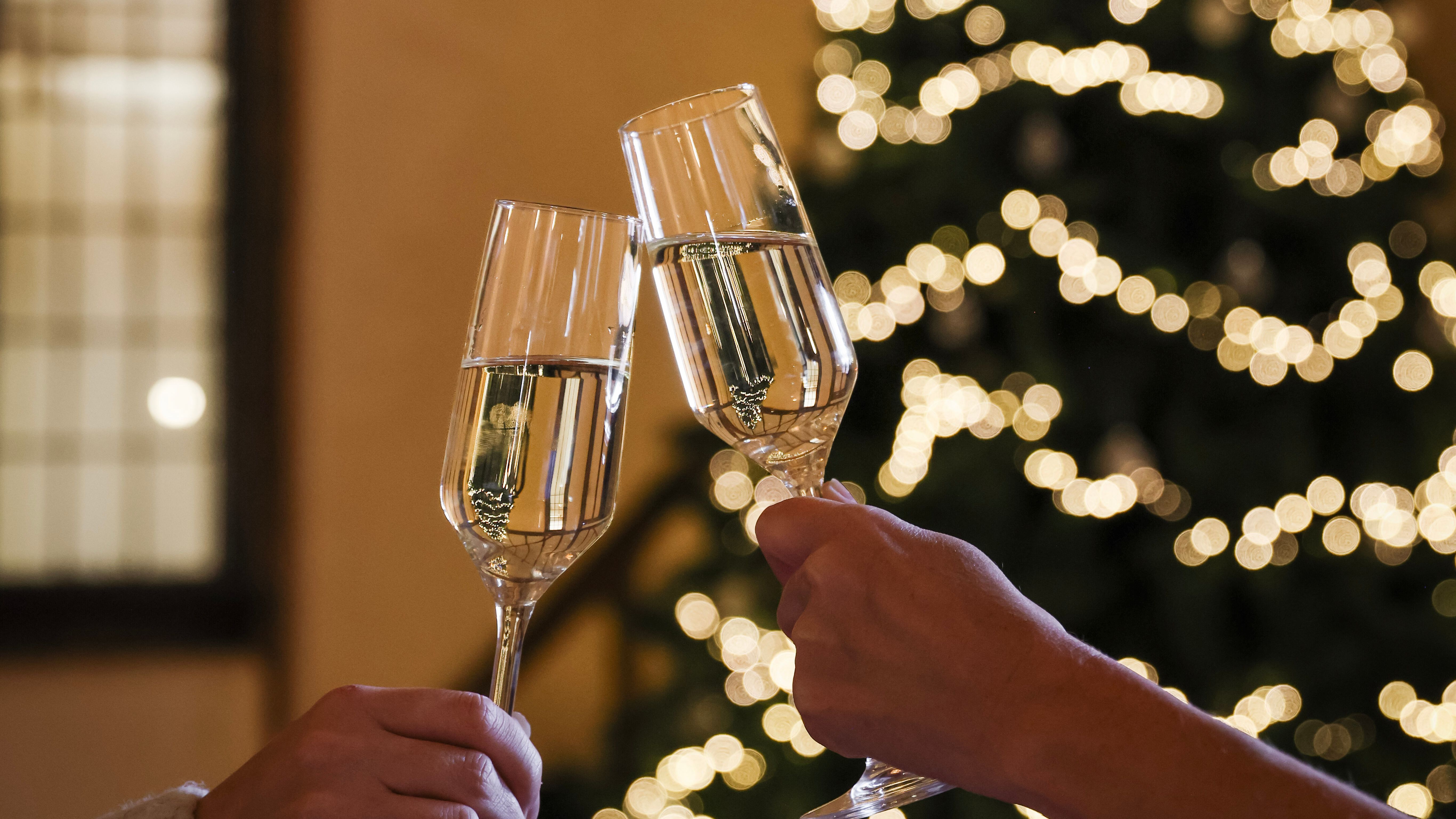 Two people clinking champagne glasses in front of a decorated Christmas tree with fairy lights.