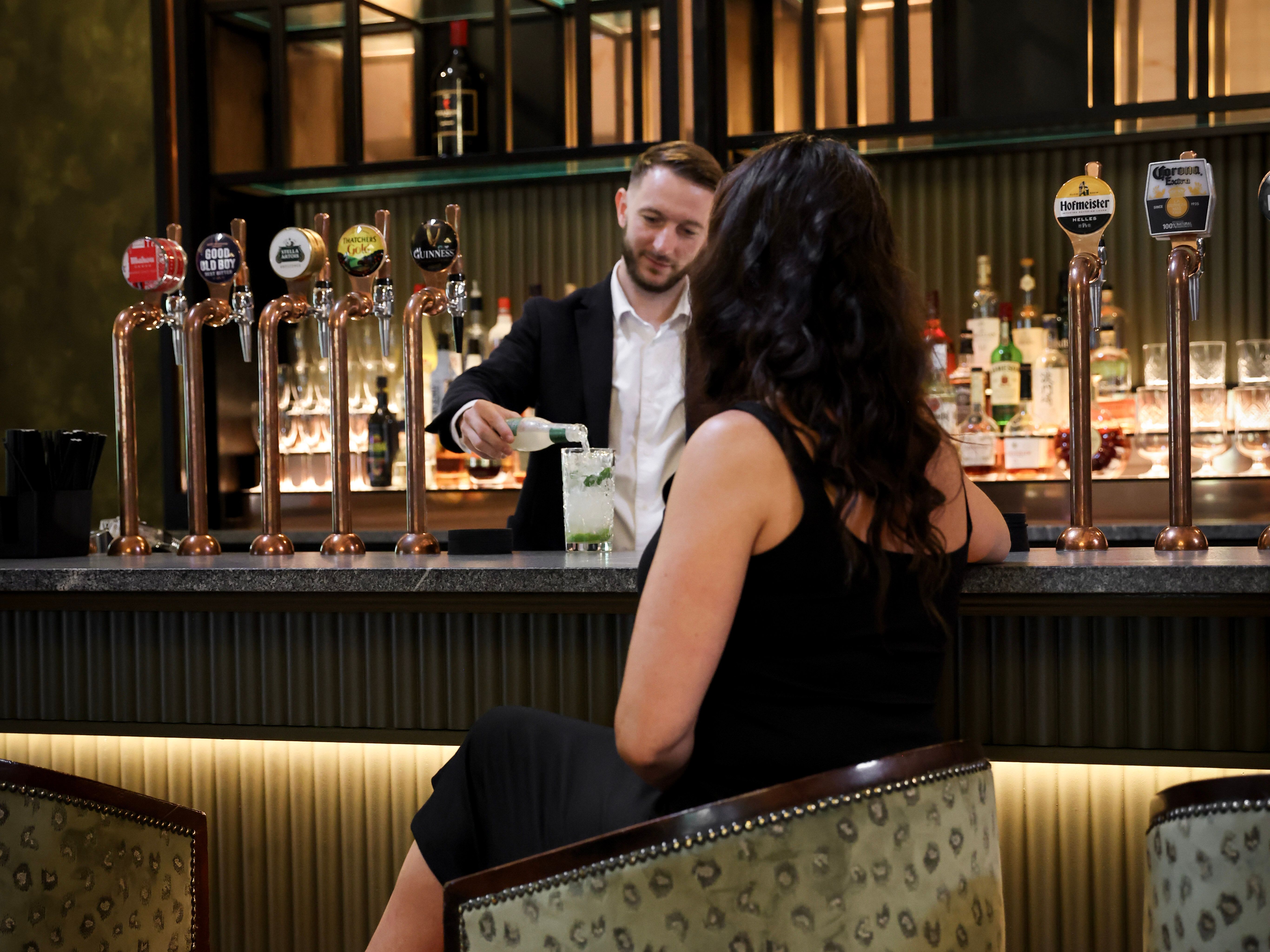 Bartender serving a cocktail to a woman sitting at a bar.